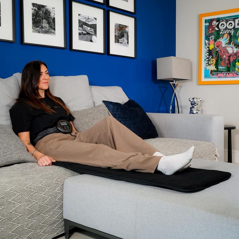 Women sat on full body mat with CELLER8 on stomach on sofa